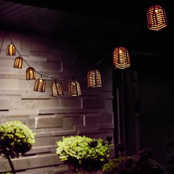 Solar rattan lantern string lights glowing against a house wall at night